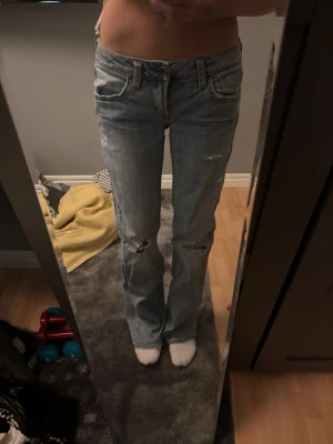 Ljusblå bootcut jeans med slitningar - Säljer ett par ljusblå bootcut jeans med slitningar på knäna och lätt tvättad look. Jeansen låg midja. Jag är 169 och dom är lite långa på mig-använt ett fåtal gånger men man ser defekter längst ner på jeansen. Om du är intresserad hör av dig för mer bilder. 