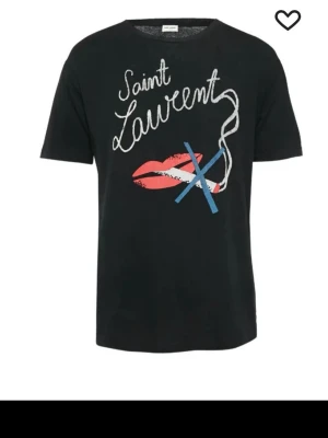 Svart Saint Laurent t-shirt med tryck - Snygg svart t-shirt från Saint Laurent med coolt tryck framtill som visar röda läppar, blått kryss och vit text. Klassisk rund hals och korta ärmar. Perfekt för dig som vill ha en statement tee från ett ikoniskt märke. 