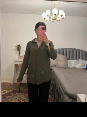 Olivgrön skjorta med krage - Snygg olivgrön skjorta med klassisk krage och långa ärmar. Skjortan har en avslappnad passform och är tillverkad i ett mjukt bomullsliknande material. Perfekt att styla med jeans eller svarta byxor för en clean look.