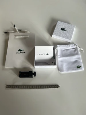 Silverfärgad klocka från Lacoste - Snygg silverfärgad klocka från Lacoste med länkarmband i metall och graverad Lacoste-logga på spännet. Klockan har ett stilrent och modernt utseende med detaljerade länkar. Kommer med originalförpackning, påse och förvaringspåse.
