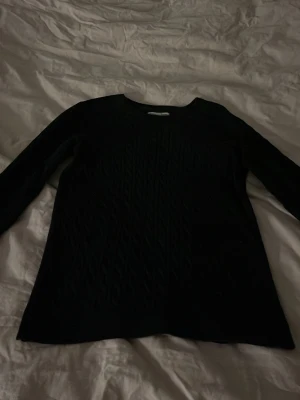 Svart kabelstickad tröja - Snygg svart kabelstickad tröja med rund hals och långa ärmar. Tröjan har ett klassiskt flätmönster framtill och är perfekt för dig som gillar en enkel men stilren look. Passar till det mesta och är superenkel att matcha. Den är perfekt och formas efter din kropp men är inte för tajt!😍😍