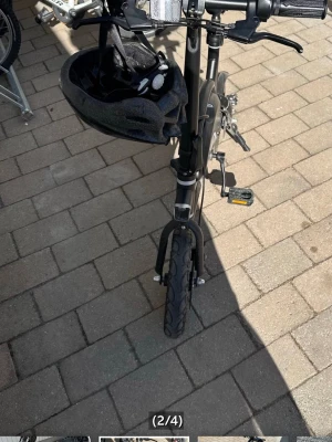 Svart elcykel med hjälm - Säljer en kompakt svart elcykel med hopfällbar ram och små hjul. Cykeln har en svart sadel, handbromsar och medföljande svart cykelhjälm. Perfekt för smidig pendling i stan och enkel att ta med på tåget. SKICKAR INTE VARAN!