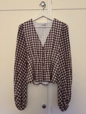Rutig blus från Adoore - Trendig brun och vit rutig blus från Adoore med v-ringning och knappar framtill. Aldrig använd💕