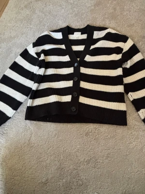 Svartvit randig kofta med knappar - Snygg stickad kofta med breda svarta och vita ränder. Koftan har djup V-ringning, fyra stora knappar framtill och långa ärmar. Perfekt för lager-på-lager och ger en cool, avslappnad vibe till din outfit.Skriv privat för fler bilder❤️
