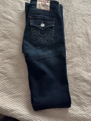 Jeans True Religion - Säljer ett par mörkblå bootcut jeans från True Religion. Dom heter Becca och är midrice. Passar mig i längden är ca 174cm. Storlek 24. Använda fåtalgånger, nypris 1300kr