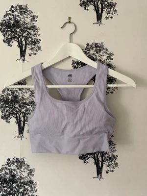 Ljuslila sport-bh från H&M - Snygg ljuslila sport-bh från H&M med ribbad struktur och brottarrygg. Tillverkad i stretchigt material som ger bra stöd under träningen. Perfekt för gymmet eller yoga och har en modern, enkel design.