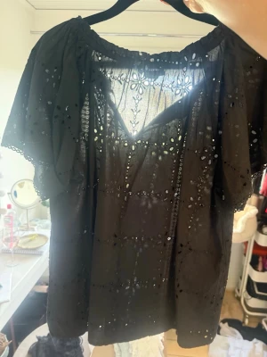Svart broderad blus med kort ärm - Säljer en svart blus med broderade hålmönster och korta puffärmar. Blusen har en rundad resårkrage och dekorativa spetsdetaljer längs kanterna. Tillverkad i tunn bomull som ger en luftig känsla och bohemisk look.