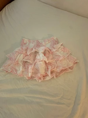 Rosa volangkjol med blommönster - Söt kortkjol med flera volanger i vitt och ljusrosa blommönster. 