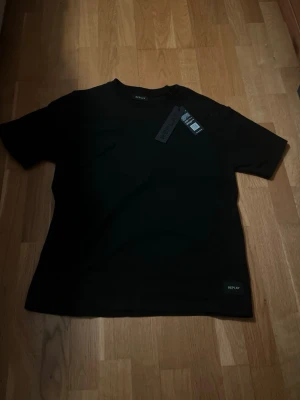 Svart t-shirt från Replay - En stilren svart t-shirt från Replay med klassisk passform och rund hals. T-shirten har korta ärmar och en diskret Replay-logga nertill på framsidan. Perfekt basplagg till garderoben.