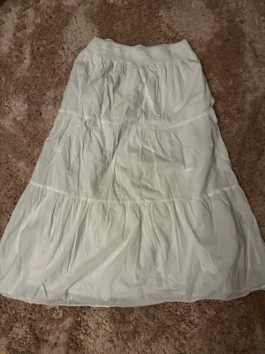 Vit långkjol från MNG - Säljer en vit långkjol från MANGO med smock i midjan och flera volanger.