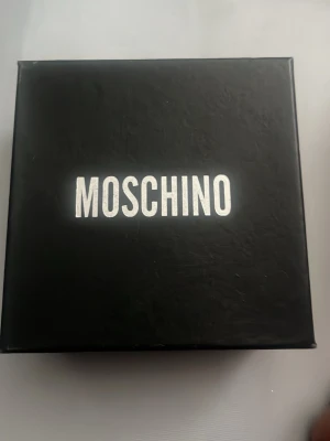 Svart Moschino presentask - Snygg svart presentask från Moschino med stilren vit logga på locket. Perfekt för att förvara accessoarer eller ge bort som present. Boxen är fyrkantig och gjord i hård kartong med matt finish.