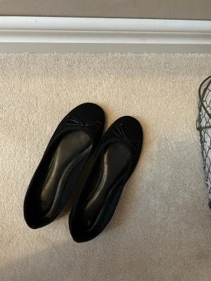 Svarta ballerinaskor med rosett - Stilrena svarta ballerinaskor med en söt liten rosett framtill. Skorna är storlek 36 men passar 37 skulle jag säga. Aldrig använda då dem är förstora 