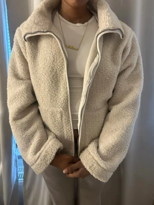 Beige teddyjacka med dragkedja - Mysig beige teddyjacka med hög krage och dragkedja framtill. Jackan har en loose passform och är tillverkad i fluffigt teddy-material som håller dig varm under kyliga dagar. Perfekt för dig som vill ha en enkel men trendig look. Ändvänd kanske 2-3 gånger, och varan är från Gina tricot i storlek S. PRIS KAN DISKUTERAS 