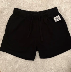 Svarta shorts med snörning från Andy - Svarta shorts ”Andy” av Frank Dandy. Fickor i sidorna, se bild nr 4. Resår och dragsnören i midjan. Storlek M. Lappen bortklippt så se måtten; Innerbenlängd 11 cm. Hellängd 34 cm. Benvidd/slut 29 cm.