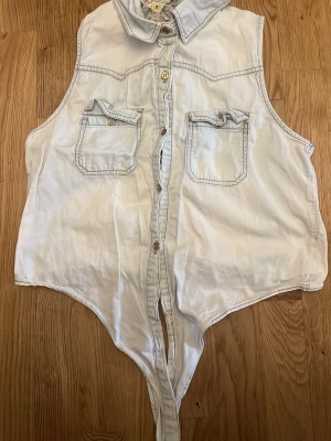 Vit skjort väst med fickor - Snygg vit skjort väst i jeans material med krage och två bröstfickor med knappar. Stängs med knappar framtill och har en unik skärning nedtill. Perfekt att styla till jeans eller kjol för en cool look.
