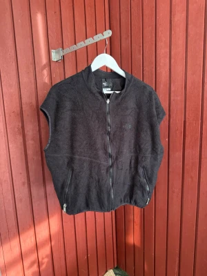 Svart fleeceväst från The North Face RARE - Ovanlig svart fleeceväst från The North Face med hel dragkedja framtill och två fickor med dragkedja. Västen är ärmlös och har en enkel, sportig design som passar perfekt för lager-på-lager-stil. Mjuk och skön fleece som håller dig varm under kyliga dagar.