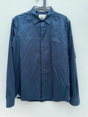 Mörkblå skjorta från Tailored Originals - Mörkblå skjorta från Tailored Originals i slim fit-modell. Skjortan har klassisk krage och knappar framtill. Insidan av kragen har ett diskret blommigt mönster. 