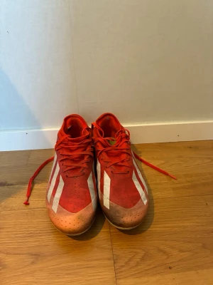 Adidas X Crazyfast fotbollsskor - Skorna är lite söndriga man kan se de i sista två bilderna.                                         Säljer ett par röda fotbollsskor från Adidas med klassiska vita ränder på sidorna. Skorna har snörning och låg profil, samt dobbar för spel på gräs. Tillverkade i syntetmaterial för bra grepp och kontroll på planen. Perfekta för dig som vill sticka ut på matchen.