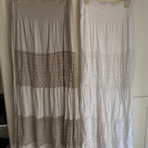 Två långa kjolar med spetsdetaljer - Säljer två romantiska långkjolar i vitt och beige med breda spetsdetaljer och volanger.  Båda har elastisk midja för skön passform.  100kr för båda eller 50kr st !!! 💕💕