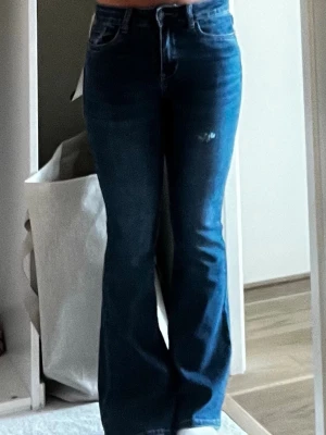 Blå bootcut jeans med hög midja - Snygga blå bootcut jeans med hög midja och klassisk femficksdesign. Jeansen har en lätt utsvängd passform nertill och subtila slitningar framtill. Perfekta att ha en lite större tröja till. De är ifrån R.Display. De har aldrig kommit till användning och har fortfarande prislapp på. 