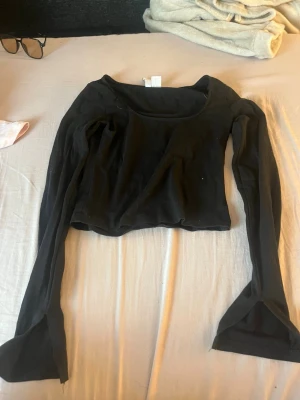 Svart croppad topp från H&M Divided - Svart långärmad croppad topp från H&M Divided. Toppen har en rund halsringning och är tillverkad i mjuk bomull, perfekt att styla med höga jeans eller kjol. Enkel och stilren design som funkar till många olika looks.