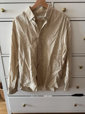 Beige linneskjorta från These Glory Days - Säljer en stilren beige skjorta från These Glory Days i mjukt linne. Skjortan har klassisk krage, knappar framtill och långa ärmar. Perfekt för dig som gillar en avslappnad men ändå snygg look.