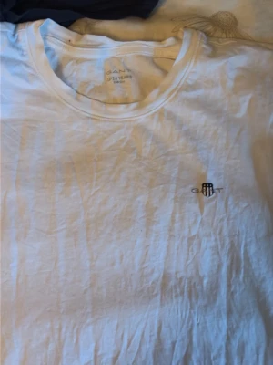 Två GANT t-shirts med logga - Säljer två stilrena t-shirts från GANT, en vit och en marinblå. Båda har rund hals och den klassiska GANT-loggan broderad på bröstet. Perfekta basplagg i mjuk bomull som funkar till det mesta.