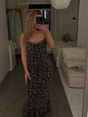 Lång leopardmönstrad klänning - Säljer en lång, figurnära klänning med leopardmönster. Klänningen har tunna axelband och en söt, lätt draperad urringning. 