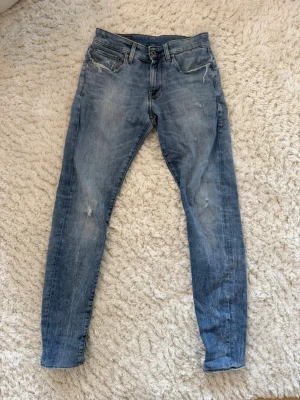 Ljusblå slim fit jeans från G star - Snygga ljusblå slim fit jeans från G star med slitningar och tvättade detaljer. Klassisk femficksmodell med dragkedja och knapp i midjan. Perfekta för en avslappnad och trendig look. Ny pris ca 1800kr, Hör av dig vid frågor!