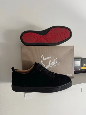 Christian Louboutin svarta sneakers - Svarta sneakers från Christian Louboutin med klassisk röd sula och ovandel i mocka. Snygg och stilren design med svarta skosnören och diskreta detaljer. Perfekta för dig som vill ha något exklusivt och trendigt i garderoben.
