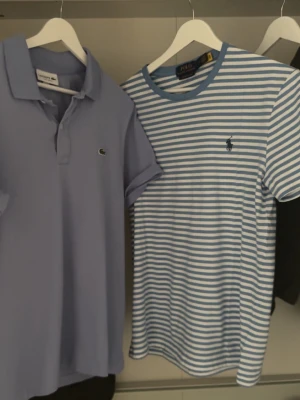 Randig t-shirt från Polo Ralph Lauren - Snygg t-shirt från Polo Ralph Lauren med blå och vita ränder. Klassisk passform med korta ärmar och rund halsringning. Ikoniska loggan broderad på bröstet. Perfekt för en avslappnad och stilren look.