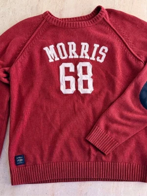 Röd tröja från Morris med tryck - Röd tröja från Morris i 100% bomull med vita bokstäver och siffror 'MORRIS 68' på bröstet. Tröjan har ribbade muddar och mörkblå armbågslappar. Perfekt för en sportig och avslappnad stil. Storlek Medium. Pris kan diskuteras 