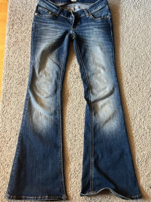 Blå bootcut jeans från 157 - Snygga blå bootcut jeans från 157 med klassisk femficksdesign och slitningar framtill. Jeansen har låg midja och utsvängda ben, perfekt för en avslappnad och trendig look. Materialet är mjuk denim med lite stretch för extra komfort.