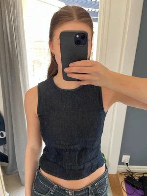 Mörkblå topp i denim - Snygg topp i mörkblå denim-look med rund halsringning och figurnära passform. Säljer då den tyvärr har blivit lite förliten 