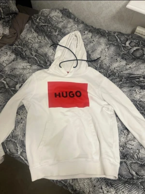  Hugo hoodie - Säljer en vit hoodie från Hugo med en stor röd ruta och svart logotyp på bröstet. Hoodien har huva med snören och en klassisk magficka. Perfekt för dig som gillar stilrena plagg med tydlig branding.