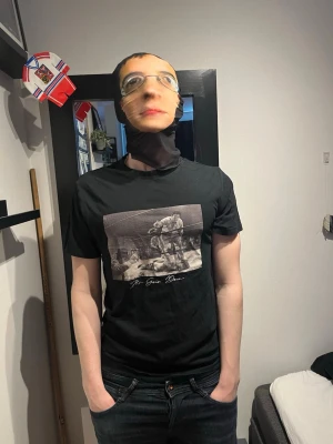 Svart t-shirt med boxningsmotiv - Svart t-shirt med tryck av en klassisk boxningsmatch på bröstet och texten 'After Game Down' under motivet. T-shirten har rund hals och korta ärmar, perfekt för en avslappnad stil. Modellen är 182 och väger 75 kg