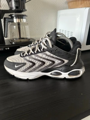 Nike Air Max TW svart/vit sneakers - Nike Air Max TW sneakers i svart och vitt med vågigt mönster på sidan, synlig Air Max-dämpning i sulan och mesh-överdel för bra ventilation. Snygga kontrastdetaljer och klassisk Nike-logga på sidan. Perfekta för dig som gillar sportig och modern stil.