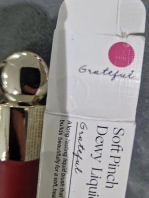 Rare Beauty Soft Pinch Dewy Liquid Blush - Flytande rouge från Rare Beauty i nyansen Grateful, en djup röd färg. Kommer i en frostad glasflaska med guldfärgat lock och applikator. Ger en daggig finish och är lätt att bygga upp för ett fräscht resultat.
