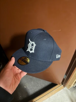 Mörkblå Detroit Tigers keps New Era - Säljer en mörkblå fitted keps från New Era med Detroit Tigers-logga framtill i vitt. Klassisk 59FIFTY-modell med böjd skärm och broderade detaljer. MLB-logga baktill. Perfekt för dig som gillar streetwear och sportig stil. Storlek 59,6cm helt ny aldrig använd