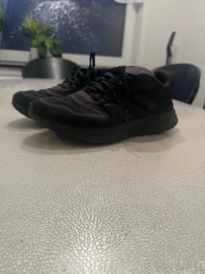 Svarta Adidas sneakers med mesh - Snygga svarta sneakers från Adidas med klassiska tre ränder på sidan. Skorna har ovandel i mesh och syntet, samt tjock sula för extra komfort. Perfekta för dig som gillar sportig stil och vill ha något som funkar till det mesta.