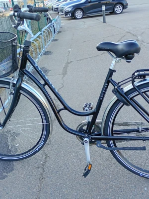 Monark svart damcykel med korg - Svart damcykel från Monark med klassisk ram, svart sadel och handtag. Utrustad med metallkorg fram, silvriga stänkskärmar och pakethållare bak. Cykeln har handbroms och är perfekt för smidiga turer i stan.
