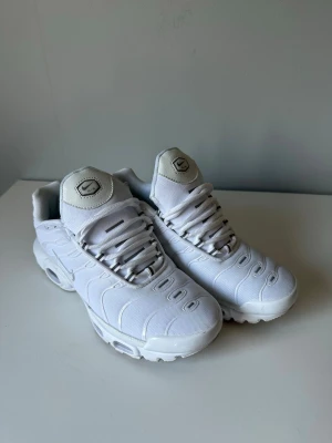 Nike tns vit - Nike Air Max Plus sneakers i helvitt med klassisk mesh-överdel och synlig Air Max-dämpning i sulan. Snyggt broderad Nike-logga på plösen och diskreta detaljer längs sidorna. Perfekta för dig som gillar en clean och sportig look.