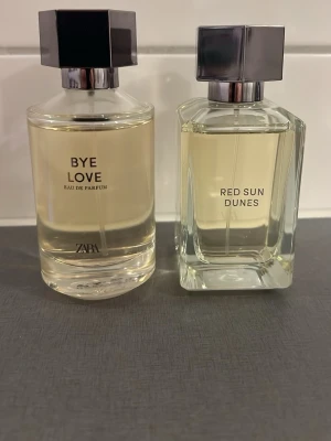 Zara Bye Love & Red Sun Dunes parfym - Två eleganta parfymer från Zara: Bye Love och Red Sun Dunes. Båda har transparent glasflaska med silverfärgad fyrkantig kork och ljusgul vätska. Modern och stilren design som passar perfekt på parfymhyllan.