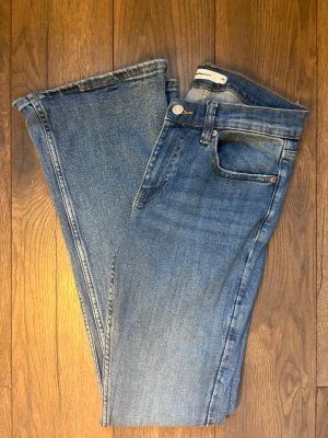 Blå bootcut jeans från Gina Tricot - Säljer ett par klassiska blå bootcut jeans från Gina Tricot. Normalhög midja och utsvängda ben. Tillverkade i mjuk denim med snygg tvätt och kontrastsömmar. Perfekta för en avslappnad och trendig look.