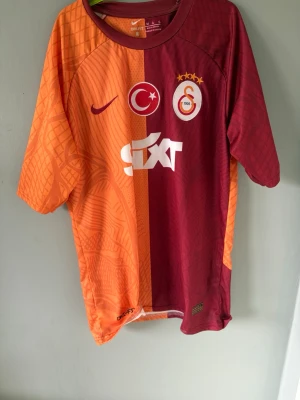 Galatasaray matchtröja Nike Icardi - Galatasaray matchtröja från Nike i röd och orange med klubbmärke, sponsortryck och nummer 9 Icardi på ryggen. Tröjan har korta ärmar, rund hals och är tillverkad i ett lätt, ventilerande material perfekt för fotboll eller träning.