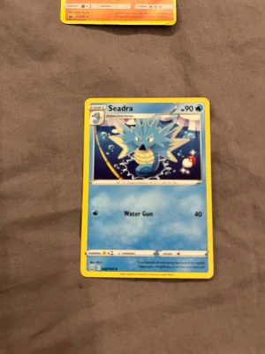 Pokémonkort Seadra - Pokémonkort med motiv av Seadra, blå och gul design med vatten-tema. Kortet har attacken Water Gun och HP 90. Perfekt för samlare eller Pokémon-fans som vill utöka sin kortsamling.