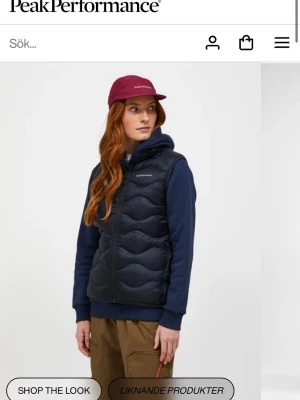 Svart dunväst från Peak Performance - Svart dunväst från Peak Performance i modellen Helium Down Vest Dam. Västen har en sportig look med quiltat mönster, hög krage och dragkedja framtill. Tillverkad i lätt och smidigt material med dunfyllning för extra värme. Perfekt för lager-på-lager-stil.