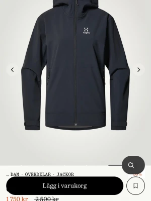 Svart vindjacka från Haglöfs med huva - Stilren svart vindjacka från Haglöfs med hel dragkedja, justerbar huva och två sidofickor med dragkedja. Jackan har minimalistisk design, diskret logga på bröstet och är tillverkad i ett lätt, vindtätt material som passar perfekt för utomhusaktiviteter. Hör av er vid fler bilder!