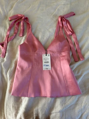 Rosa satintopp med knytrosetter - Supersöt rosa linnetopp från Zara med axelband som knyts i rosetter. Toppen har v-ringad urringning och figurnära passform. Perfekt för sommardagar och enkel att styla med jeans eller kjol.💗