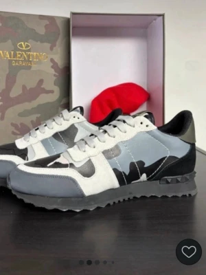 Valentino Garavani camo sneakers - Snygga sneakers från Valentino Garavani med grå, svart och vit camo-mönstrad ovandel. Skorna har detaljer i mocka och läder, svarta och vita partier samt en robust sula med nitar vid hälen. Perfekta för dig som vill sticka ut med exklusiv streetstyle oanvändtbar. 